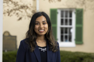 An environmental portrait of Priyanka Parikh on the porch of the chapel with Demosthenian Hall in the background.