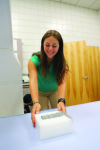 Peyton Macik smiles while placing a bone scan sample into lab imaging equipment.